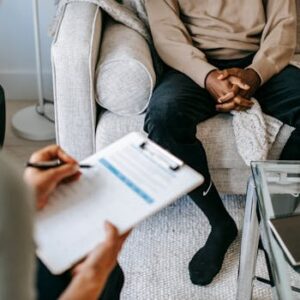 Therapist takes notes as client sits on a sofa during a psychotherapy session.