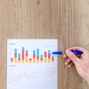 A hand points a pen at business graphs on a wooden table, highlighting data analysis.