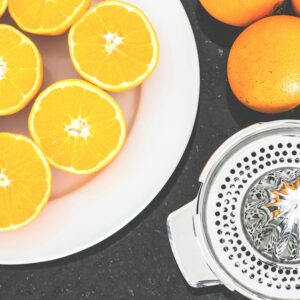 Top view of fresh oranges sliced on a white plate with a metal juicer nearby.