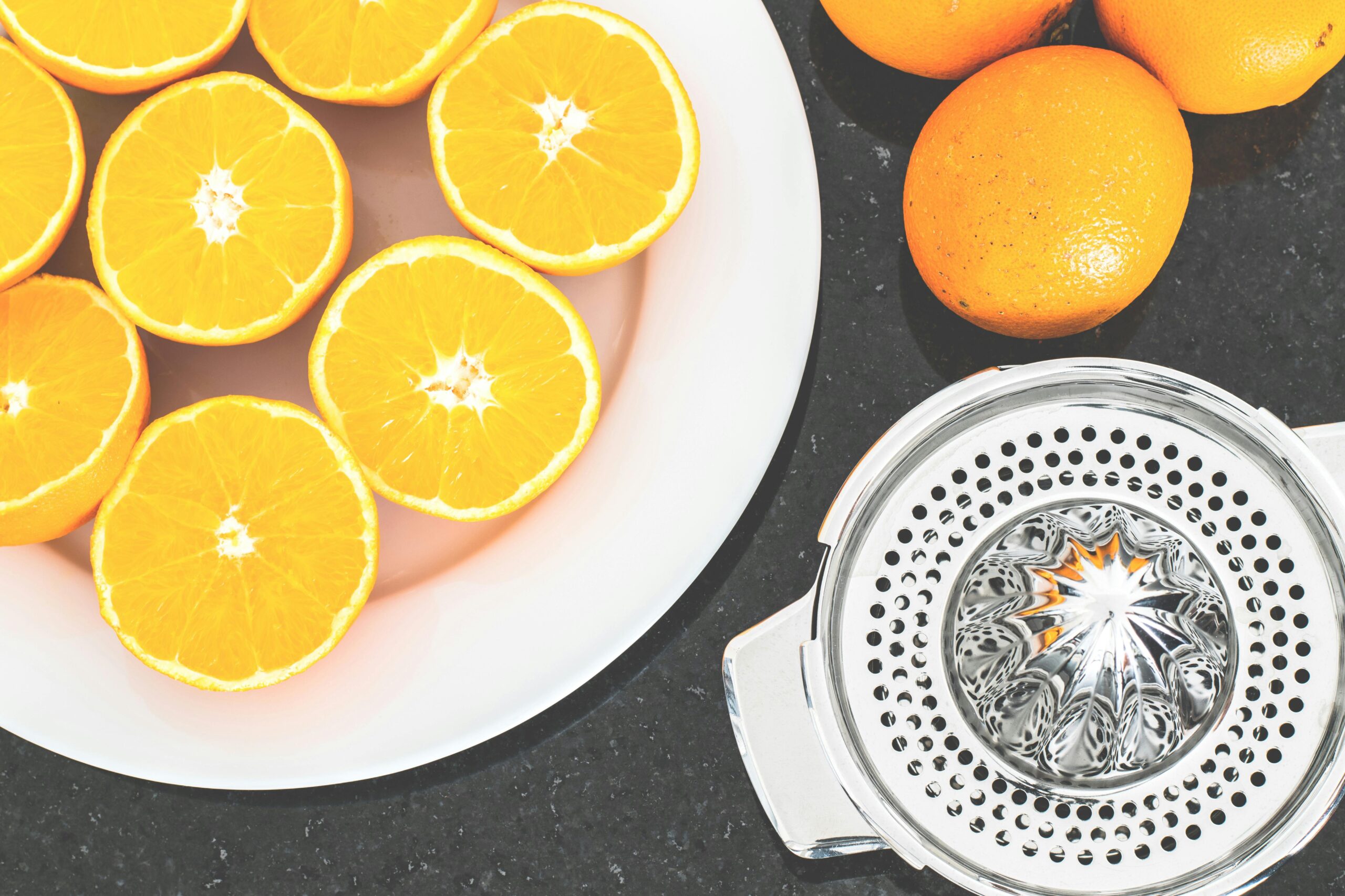 Top view of fresh oranges sliced on a white plate with a metal juicer nearby.