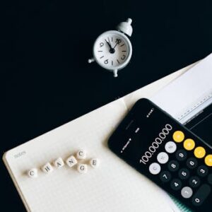 Notebook with an iPhone displaying 100,000,000, desk clock and financial charts suggesting market analysis.