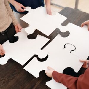 Four people collaborate by assembling large white puzzle pieces on a table.