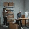 Two workers handling packages and organizing stock in a warehouse setting.