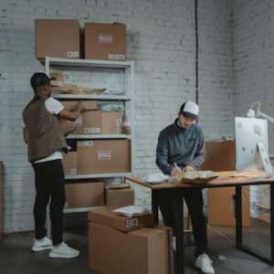 Two workers handling packages and organizing stock in a warehouse setting.