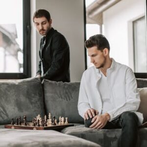 Two men playing chess on a couch, focusing on strategy inside a modern living room.