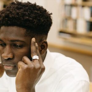 A contemplative man with fingers on temples, pondering in a library.