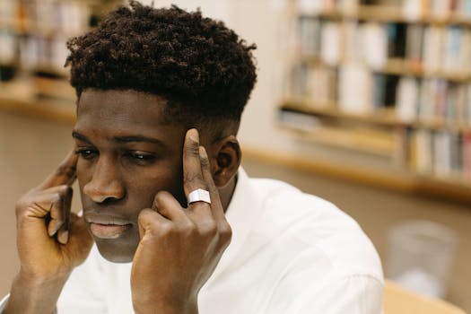 A contemplative man with fingers on temples, pondering in a library.