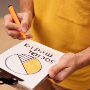 Person draws a social media pie chart on clipboard with orange marker.