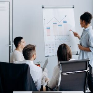 Business team in meeting with presenter discussing charts on a flip board.
