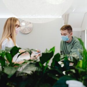 Reception area in a healthcare facility with masked staff and patients interacting indoors.