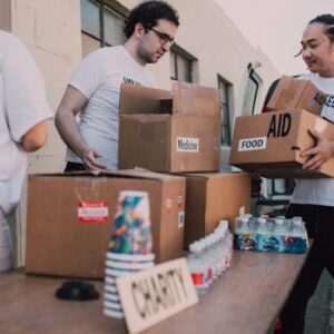 Volunteers loading aid boxes with food and medicine from a van outdoors.