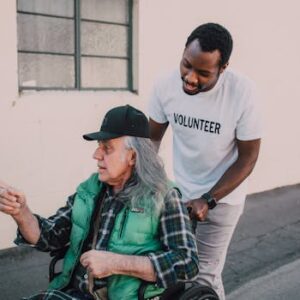 A volunteer helps an elderly man in a wheelchair outside, showing community support and care.