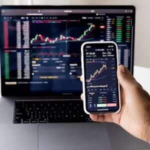 Person checking stock market graphs on laptop and smartphone, focusing on financial data.