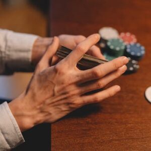 Hands holding cards and poker chips on a wooden table, capturing the gaming atmosphere.