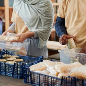 Adults sorting food donations in containers for charity. Community service effort indoors.