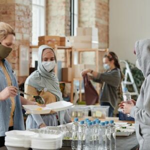 A diverse group of volunteers prepare and distribute food and drinks at an indoor community center.