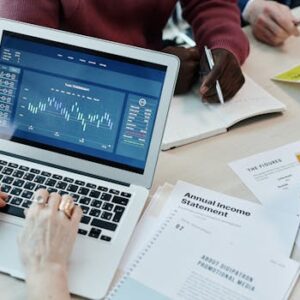 Business professionals analyzing financial data on a laptop during a meeting. Charts and reports visible.