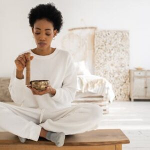 Woman practicing meditation with a Tibetan singing bowl in a serene interior setting.