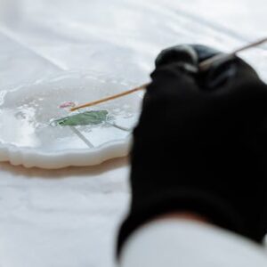 Close-up of hands crafting detailed resin art using a delicate tool, showcasing artistic precision.
