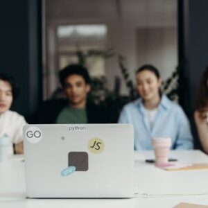 A focused group meeting in an office setting with diverse team members and a laptop featuring tech stickers.