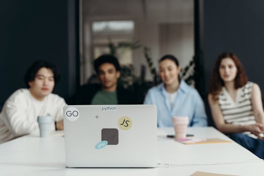A focused group meeting in an office setting with diverse team members and a laptop featuring tech stickers.