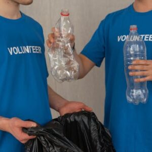 Two volunteers in blue shirts collect plastic bottles for recycling, showcasing community involvement.