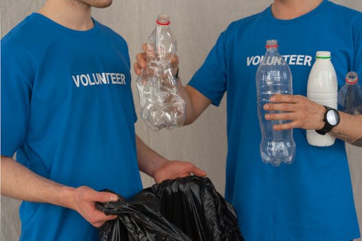 Two volunteers in blue shirts collect plastic bottles for recycling, showcasing community involvement.