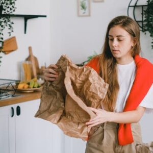 Young serious female with long hair sorting reusable paper trash in modern kitchen in apartment