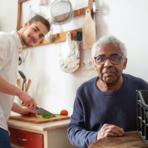 A young adult helping a senior in the kitchen, highlighting care and support at home.