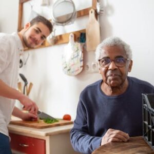 A young adult helping a senior in the kitchen, highlighting care and support at home.