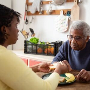 A woman assists an elderly man with meals at home, showcasing care and support.
