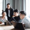 A group of Asian professionals engaged in a collaborative business meeting in a bright office setting.