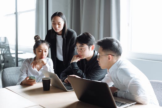A group of Asian professionals engaged in a collaborative business meeting in a bright office setting.