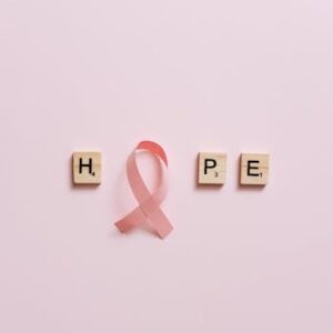 Flat lay of pink ribbon symbolizing cancer awareness with scrabble tiles spelling HOPE on a pink surface.
