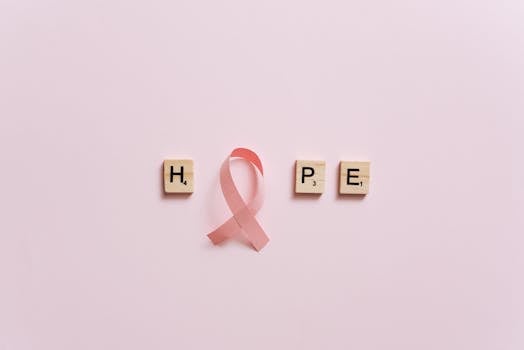 Flat lay of pink ribbon symbolizing cancer awareness with scrabble tiles spelling HOPE on a pink surface.
