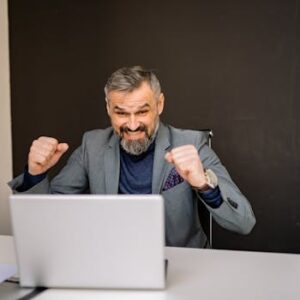 Happy businessman celebrating success while looking at laptop in modern office.