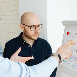 Three men discussing financial charts on a whiteboard during a business meeting.