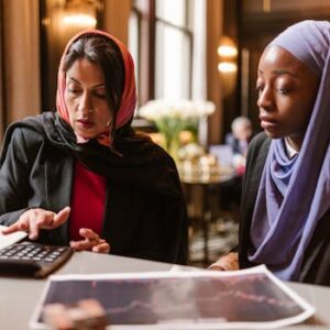 Two multicultural women collaborating on financial analysis using a calculator.