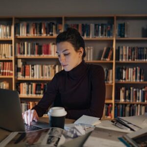 Adult woman intensely focused while working on a laptop in a library setting.