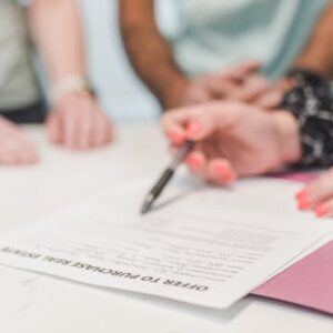 Close-up of people reviewing and signing an offer to purchase real estate document.