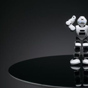 A small humanoid robot with glowing eyes on a reflective table in a dark setting.
