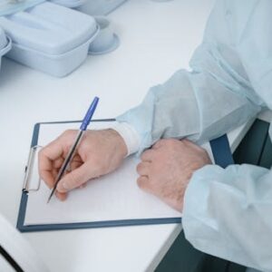 A medical professional wearing protective clothing writing on a clipboard.