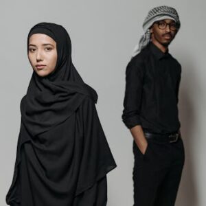 A man and woman wearing traditional Middle Eastern attire pose against a neutral background.