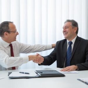 Two businessmen in a bright office seal a deal with a handshake, conveying agreement and cooperation.