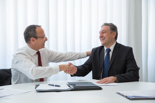 Two businessmen in a bright office seal a deal with a handshake, conveying agreement and cooperation.