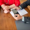 Business meeting at a wooden table with consultant reviewing documents and using a digital tablet.