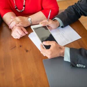 Business meeting at a wooden table with consultant reviewing documents and using a digital tablet.