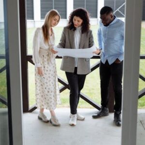 A realtor with clients examining a floor plan outside a modern property.
