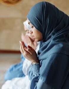 Two Muslim women in hijabs praying inside a mosque, exemplifying faith and spirituality.