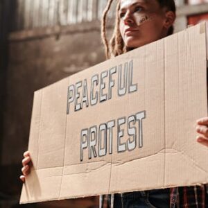 A woman holding a cardboard sign with 'Peaceful Protest' written on it inside an industrial setting.